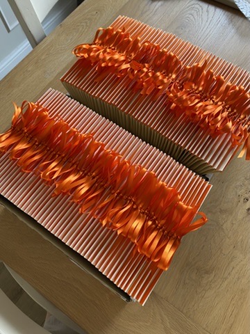 Rows of order of service booklets with hand-tied orange satin ribbons ready for cathedral wedding
